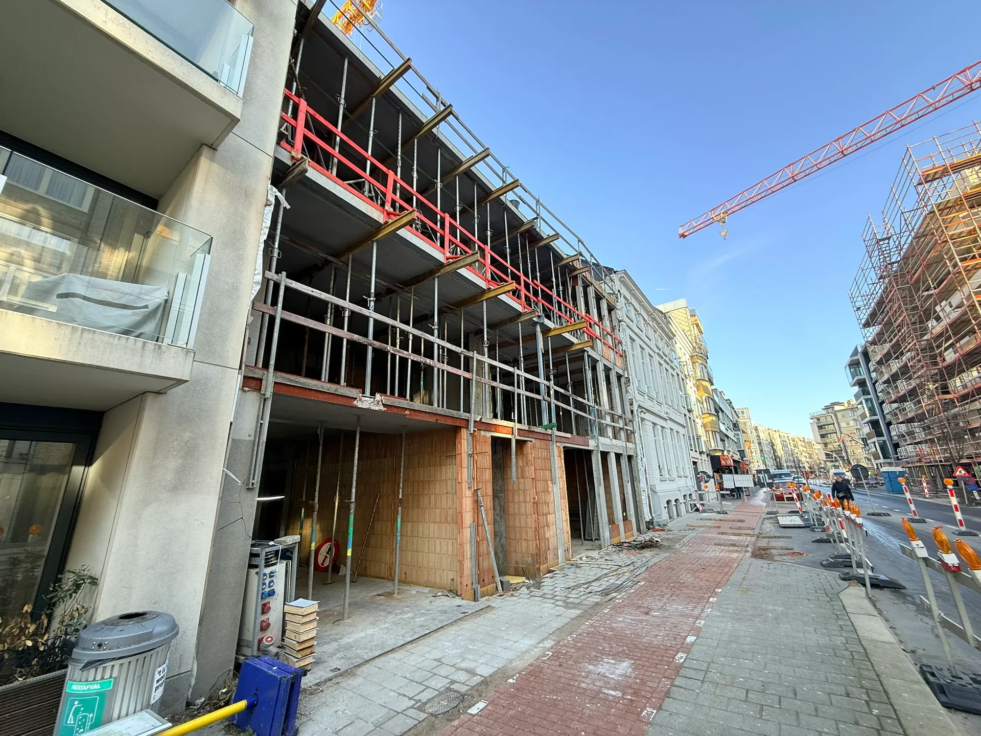 Betonnen draagstructuur van een appartementsgebouw met stempels en rode randbeveiliging in een straat met herenhuizen